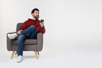 Happy man with smartphone sitting on armchair against white background. Space for text