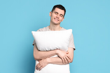 Happy man in pyjama holding pillow on light blue background