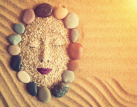 A woman's face made of stones on yellow sand. Copy space for yoru text