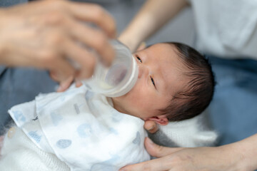 An 8-day-old baby in a Taiwanese grandmother in her 70s drinking milk in a baby bottle...