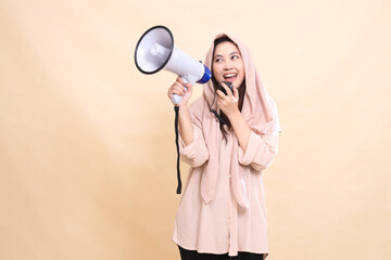 Candid indonesia woman with her right hand holding audio and carrying a megaphone (loudspeaker) shouting cheerfully to announce the announcement. young beautiful for business, technology, fashion