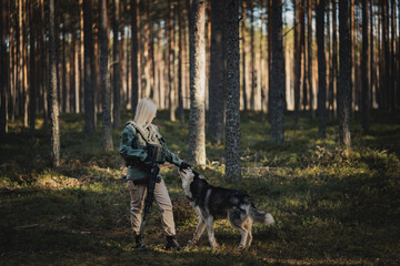 Military blonde girl with a weapon with a kind husky dog ​​in the forest.