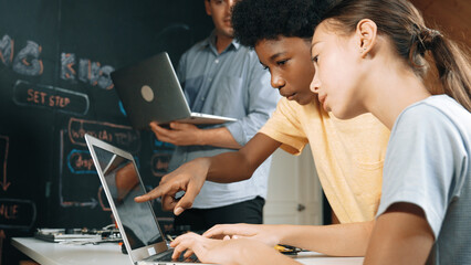 Caucasian girl programing or coding system while african boy fixing model. Teacher holding laptop...
