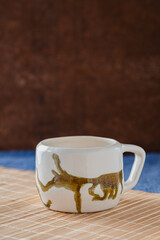 One ceramic hand painted mug on placing mat and dark brown background 