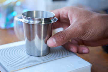 Fototapeta na wymiar A close-up image capturing the moment a person is measuring coffee in a stainless steel cup, placed on a white digital scale