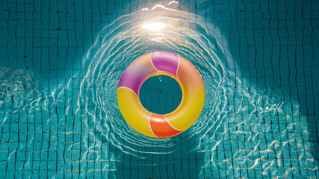 An image showing a colorful swim ring floating on the water surface of a sunlit swimming pool.
