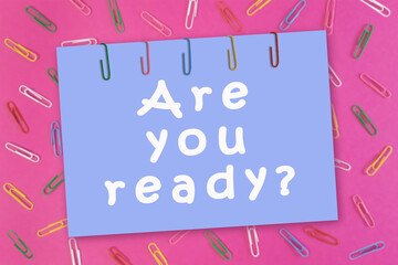 Are you ready written on blue sheet of paper on blurred pink background with paper clips. Back to school concept, preparation for the school year, new event