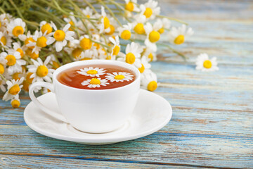 Daisy flowers in a white cup of tea, chamomile herbs on wooden background. Herbal medicine. Healthy lifestyle concept.
