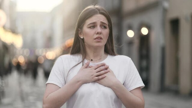 Worried young woman walking down the urban street while has panic heart attack hold hand on chest and try to calm down alone Anxious female with mental health problem outdoors