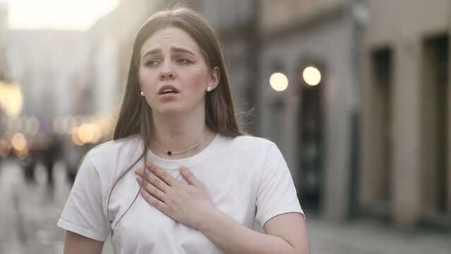 Worried young woman walking down the urban street while has panic heart attack hold hand on chest and try to calm down alone Anxious female with mental health problem outdoors