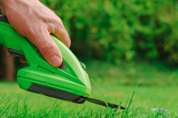 lawn trimmer. electric trimmer in a mans hand close-up cuts the grass. process of cutting grass close-up.Garden equipment and tools. - obrazy, fototapety, plakaty