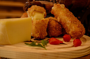 A light wooden board, with a piece of cheese, a sprig of parsley, chili pepper and crispy cheese breading.