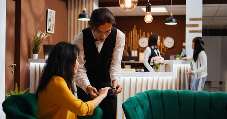 Hotel guest paying for drink and giving cash to worker, feeling happy with customer services and...