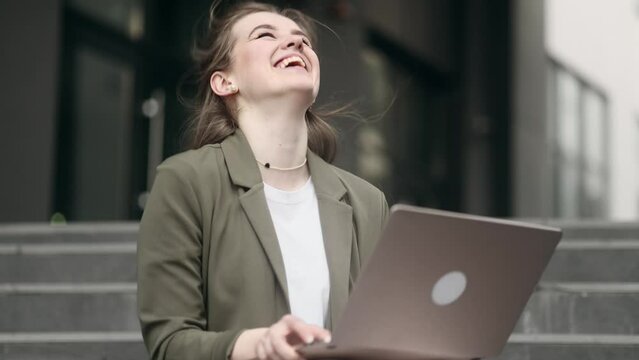Beautiful young businesswoman get notification and celebrate online win success reading great news message on laptop feel amazed happy and looking at camera showing thumbs up outdoors 
