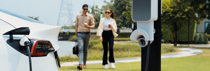 Young couple with coffee recharge EV car battery at charging station connect to electrical...