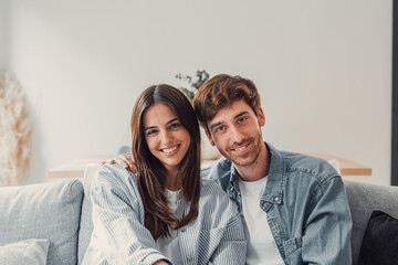 Portrait of young 20s just married couple in love posing photo shooting seated on couch in modern studio apartments, concept of capture happy moment, harmonic relationships, care and sincere feelings.