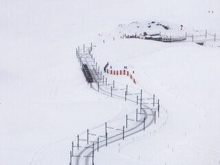 Aerial view of a snowy landscape in Zermatt, Switzerland, featuring a train track winding up the mountain and a group of people near a station, highlighting the serene beauty of the winter resort.