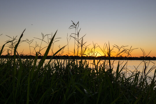 The sun hides behind the islands of the river Parana, View from the grasslands on the shore