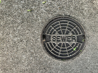 Sewer Line Plate. Circular metal sewer line plate set against a concrete street or sidewalk. Positioned to the side for copy space.