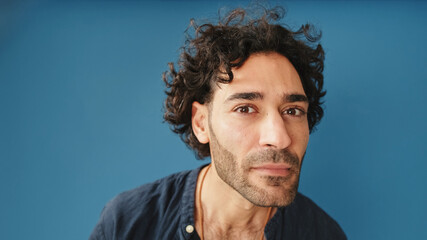 Obraz premium Close-up, man with curly hair, wearing blue shirt, looking at camera looking for something isolated on blue background in studio
