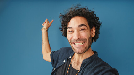 Smiling man with curly hair, wearing blue shirt, looking at camera making video call, welcome sign...