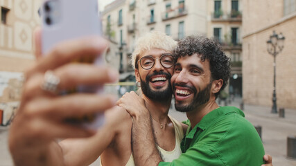 Gay couple stands hugging and makes video call from mobile phone, waving in greeting - obrazy, fototapety, plakaty