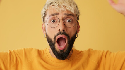 Close-up of an astonished guy with glasses, dressed in yellow T-shirt, looking at camera expressing...