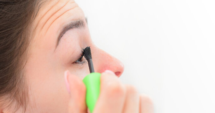 Closeup young girl applying mascara on eye lashes, with copy space