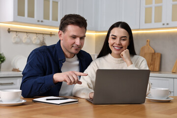 Happy couple using laptop at wooden table in kitchen