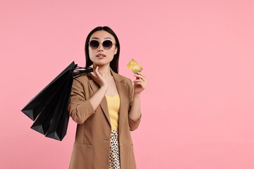Beautiful woman with shopping bags and credit card on pink background. Space for text