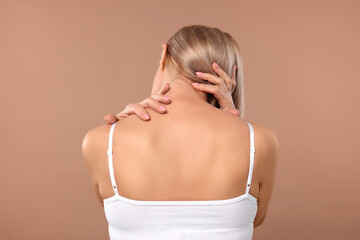 Woman suffering from pain in her neck on beige background, back view