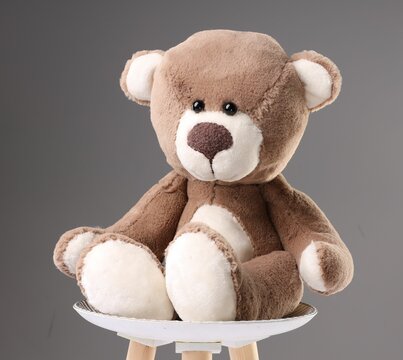Cute teddy bear on stool against grey background