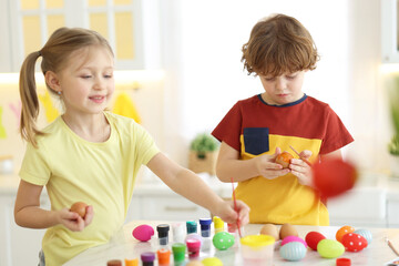 Easter celebration. Cute children painting eggs at white table in kitchen
