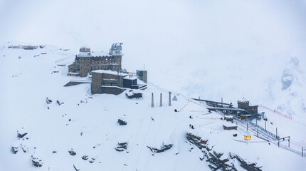 A snowy Zermatt, Switzerland from above, shows a big stone building with turrets, ski lifts, and a...