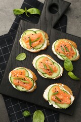Tasty canapes with salmon, cucumber and cream cheese on grey table, top view