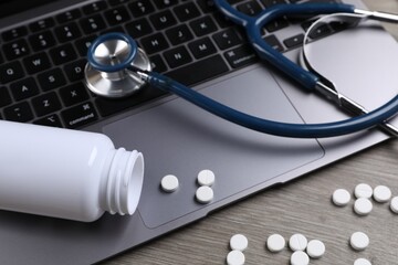 Laptop, stethoscope, pills and bottle on wooden table, closeup