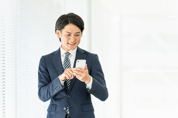 スマートフォンを操作・検索するスーツ姿の若いアジア人ビジネスマン
