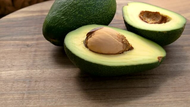 Close-up view of a whole and half avocado rotating on a wooden surface