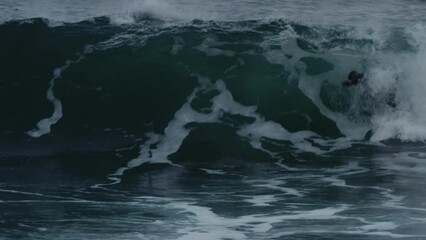 Surfer pushes on nose popping up and pulling into barrel of wave in full wetsuit skimming to cutback, slow motion