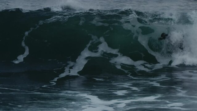 Surfer pushes on nose popping up and pulling into barrel of wave in full wetsuit skimming to cutback, slow motion