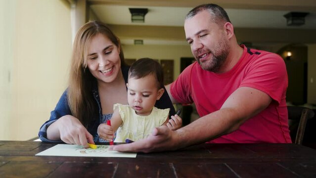 Happy Latin family having fun at home. Father, baby daughter, and mother painting together. Family concept