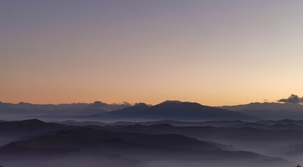 Fototapeta na wymiar Le valli sotto alle montagne al tramonto come laghi di nebbia