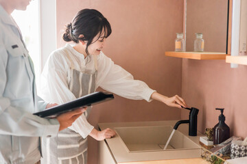 洗面所で水栓の作動確認をする主婦の女性と水道屋・設備屋の男性
