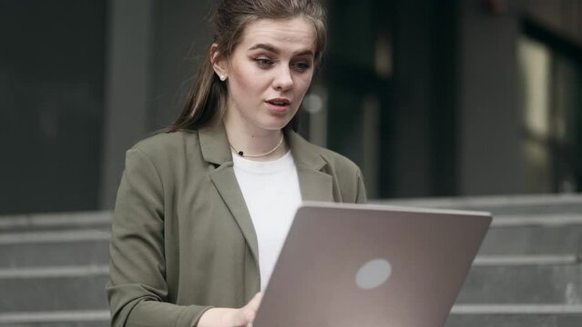 Beautiful young businesswoman get notification and celebrate online win success reading great news message on laptop feel amazed happy and looking at camera showing thumbs up outdoors 