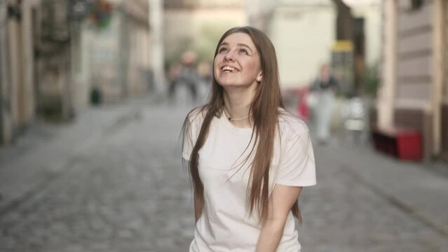 Charming young woman with long hair walking down the street turns around with flying hair outdoors Happy relaxed tourist walking on the city centre enjoying beautiful day alone