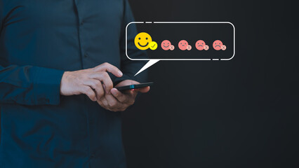 A male hand uses a mobile phone displaying a happy smile face icon to express satisfaction with the service, indicating a very impressed opinion rating. - 774526938