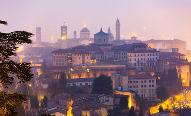 Scenic view of illuminated Bergamo upper city, historic center on hill with medieval architectural...