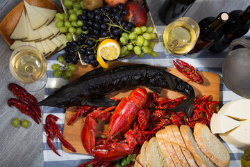 Top view of smoked sturgeon and boiled lobster with crayfishes, fruits and white wine on wooden...