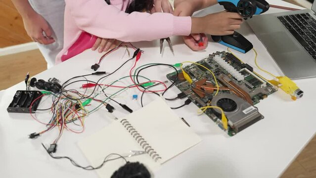 Smart teacher hand teaching students about electronic board. Girl learn about digital electrical tool and fixing motherboard at table with chips and wires placed. Focus on table. Top view. Erudition.