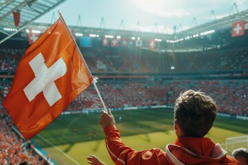 A young man holds a Swiss flag in a stadium full of people. Football fan supporting the team